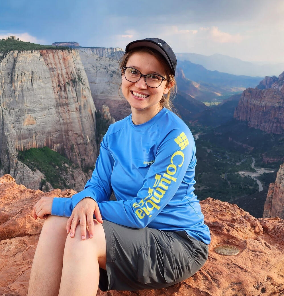 Image of Krysta Liz sitting on a rock cliff in Utah wearing outdoor gear.